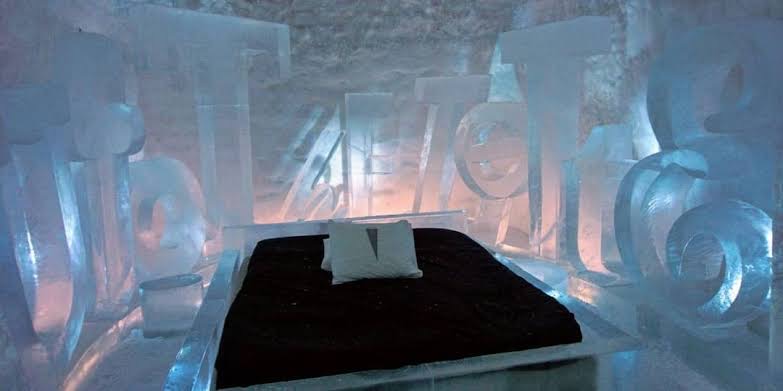 A low snow building lit from within, standing on a frozen lake at dusk.
