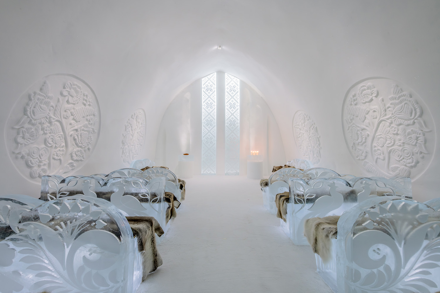 A hall of carved ice with rows of block benches facing a lit end wall.