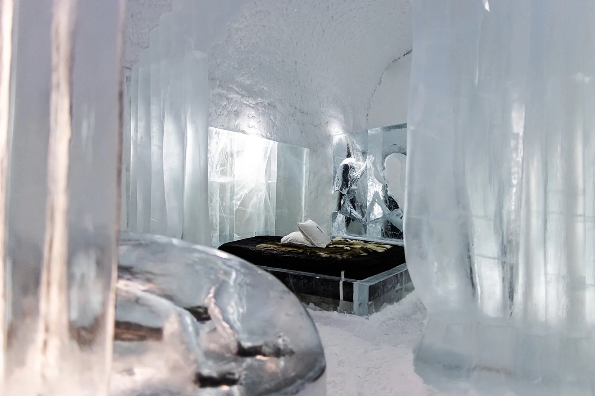 A snow-walled sleeping room lit blue, with a fur-covered bed on an ice base.